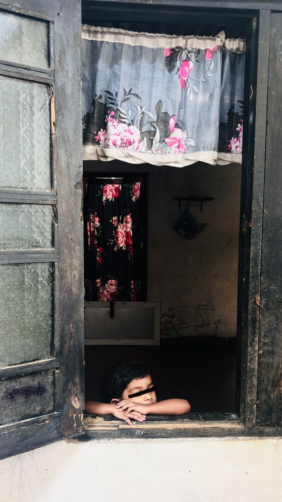 A young child resting their arms on a wooden window sill at home